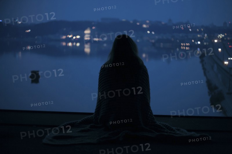 Caucasian woman sitting near waterfront at night