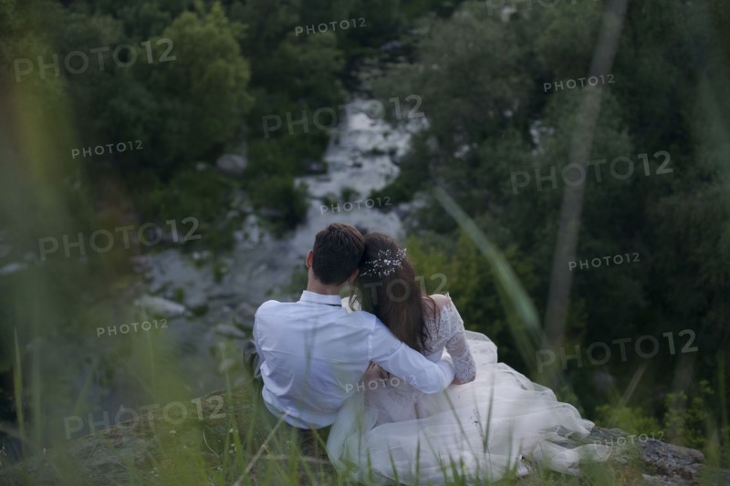 Caucasian bride and groom sitting on hill admiring river