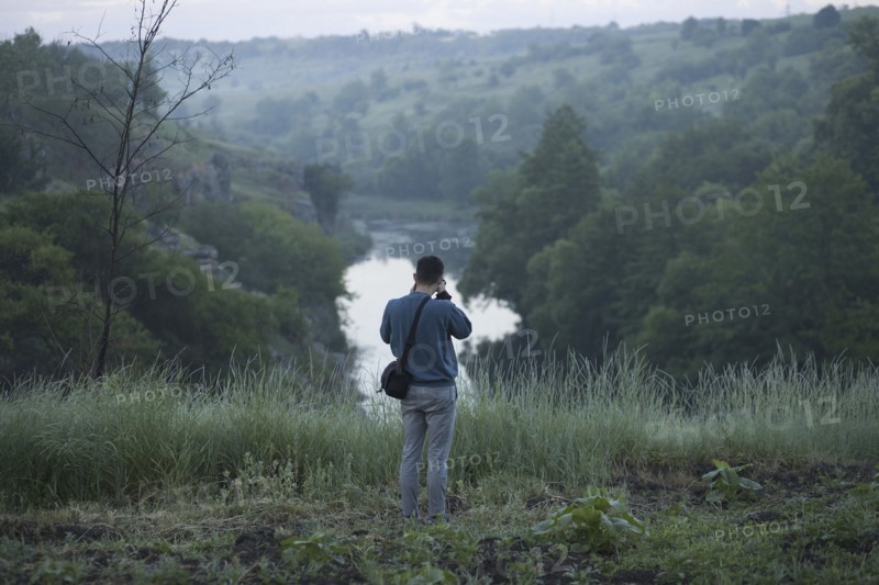 Caucasian man standing on hill photographing river