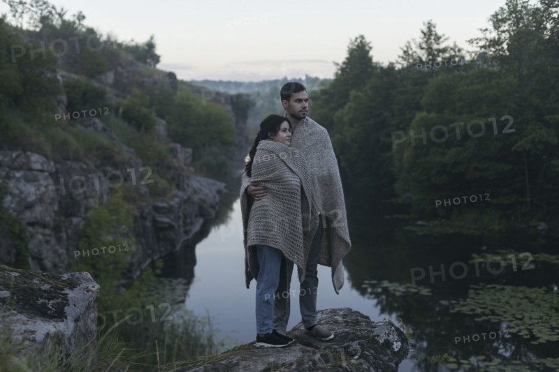Caucasian couple wrapped in blanket standing on rock near river