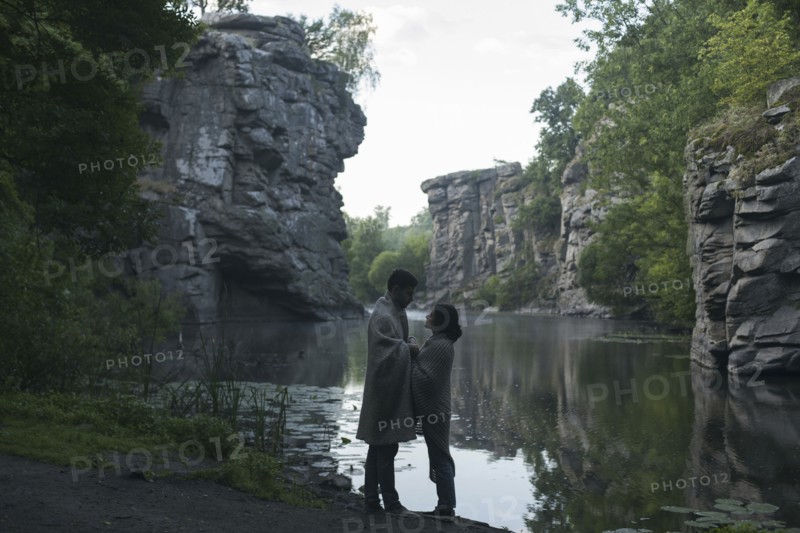 Caucasian couple wrapped in blanket holding hands near river