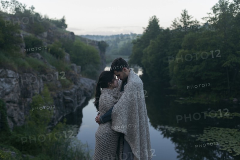 Caucasian couple wrapped in blanket hugging near river
