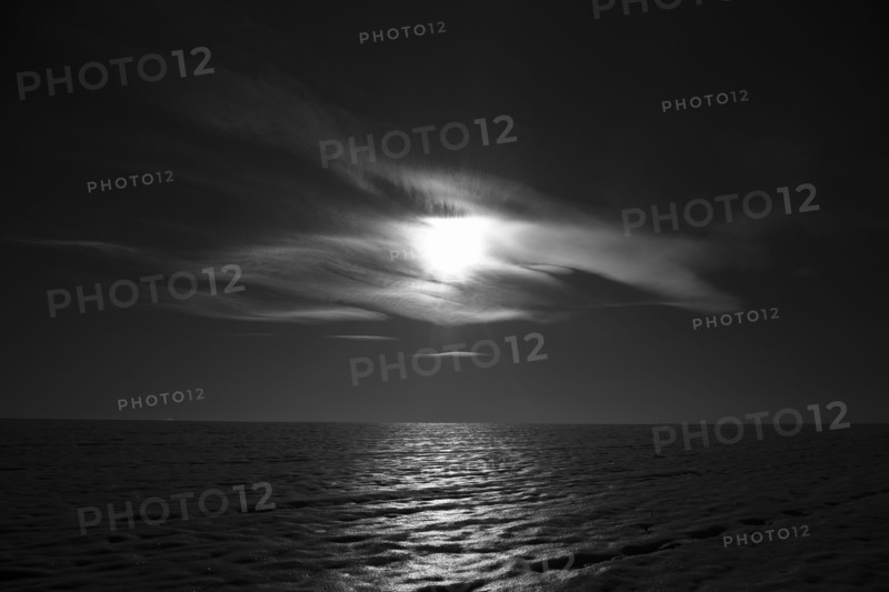 Moon shining behind cloud over ocean