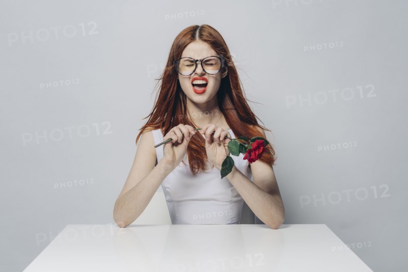 Caucasian woman sitting at windy table snapping stem of rose