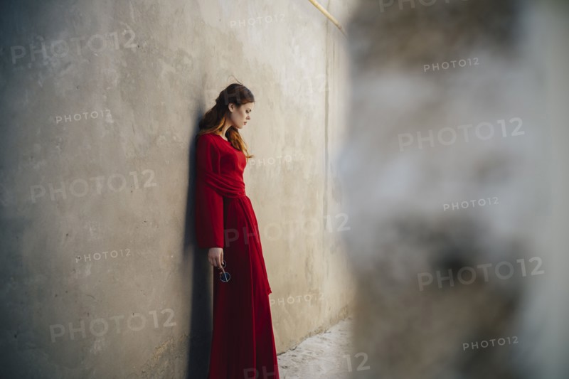 Caucasian woman wearing red dress leaning on wall in alley