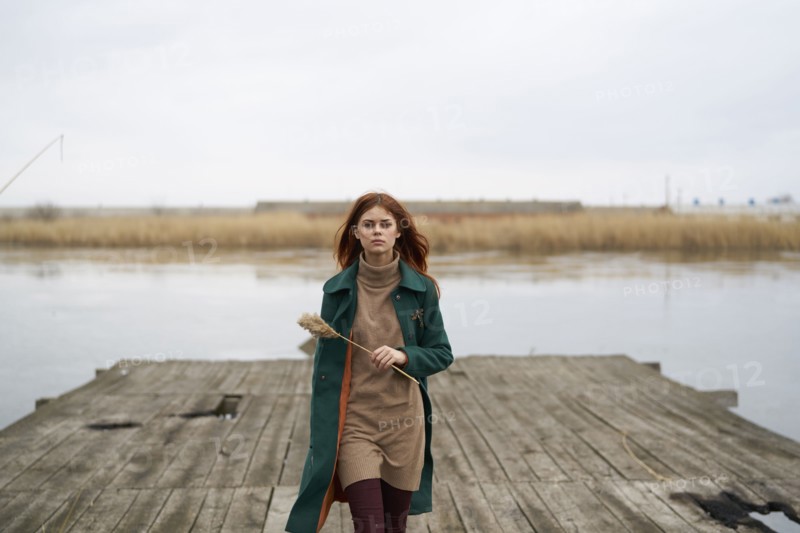 Serious Caucasian woman walking on dock holding stalk of grass
