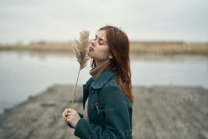 Caucasian woman standing on dock smelling stalk of grass