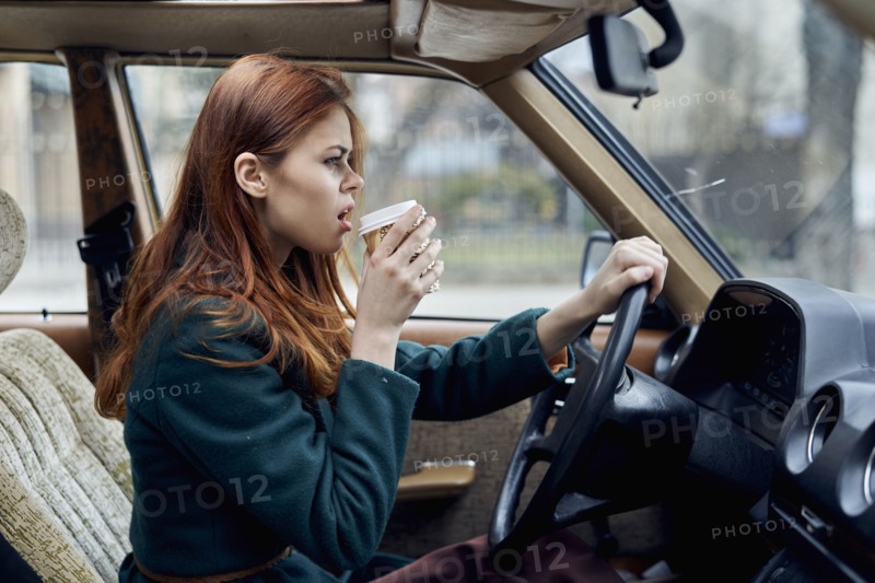 Angry Caucasian woman driving car and drinking coffee