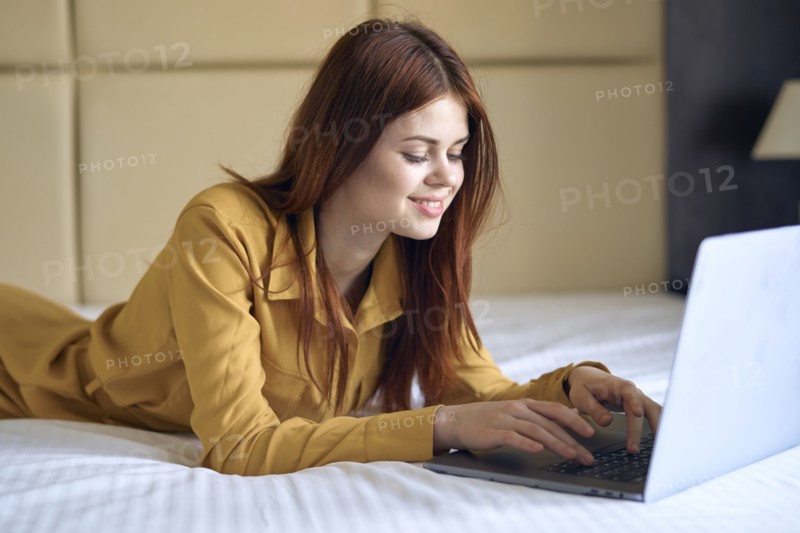 Smiling Caucasian woman laying on bed using laptop