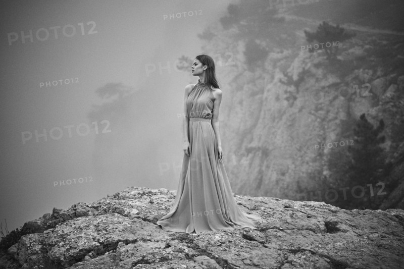 Woman wearing dress standing on rock in fog