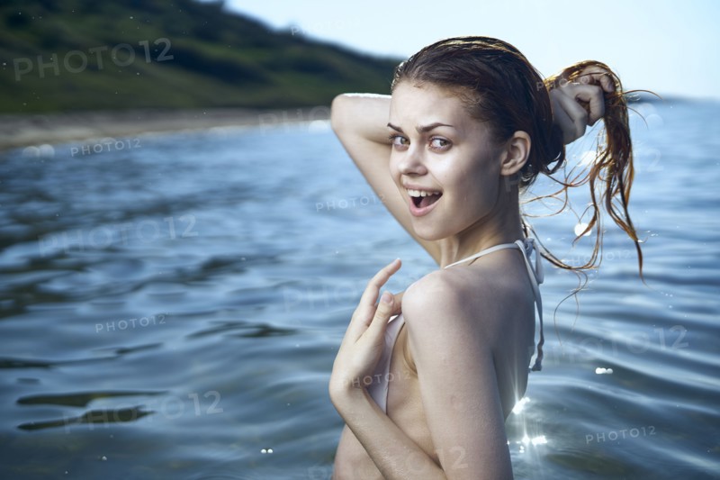 Laughing woman squeezing wet hair in ocean