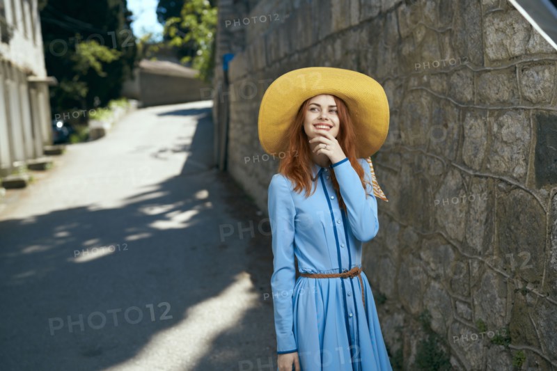 Smiling Caucasian woman wearing hat near stone wall