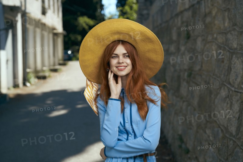 Smiling Caucasian woman wearing hat near stone wall