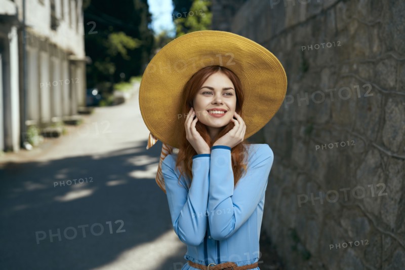 Smiling Caucasian woman wearing hat near stone wall