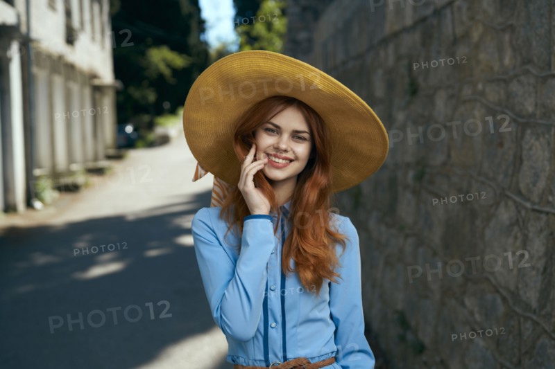 Smiling Caucasian woman wearing hat near stone wall