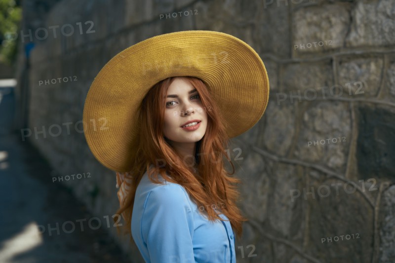 Smiling Caucasian woman wearing hat near stone wall
