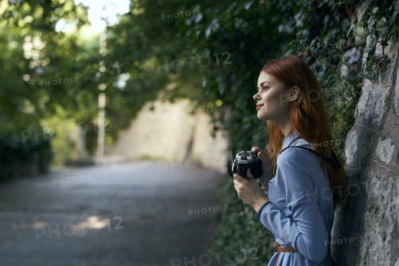 Caucasian woman photographing with camera near stone wall
