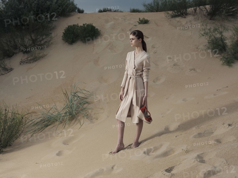 Caucasian woman wearing dress on beach carrying shoes