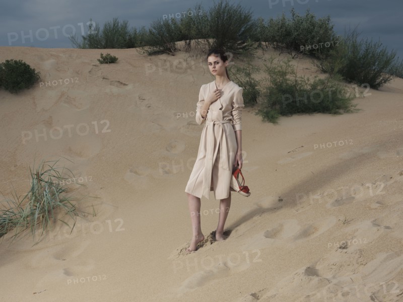 Caucasian woman wearing dress on beach carrying shoes