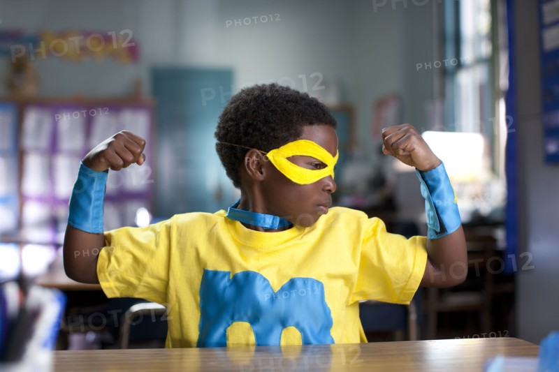 African American boy wearing superhero costume in classroom