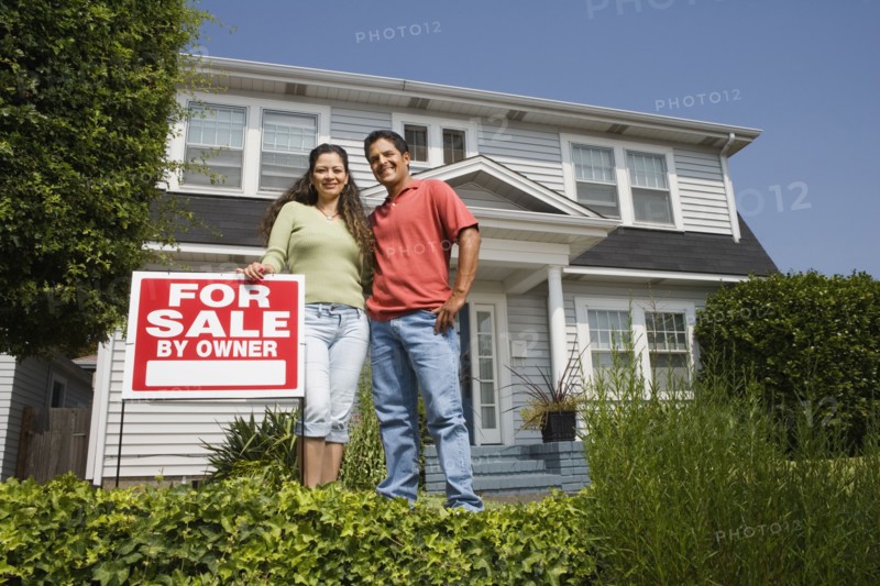 Hispanic couple with For Sale sign in front of house
