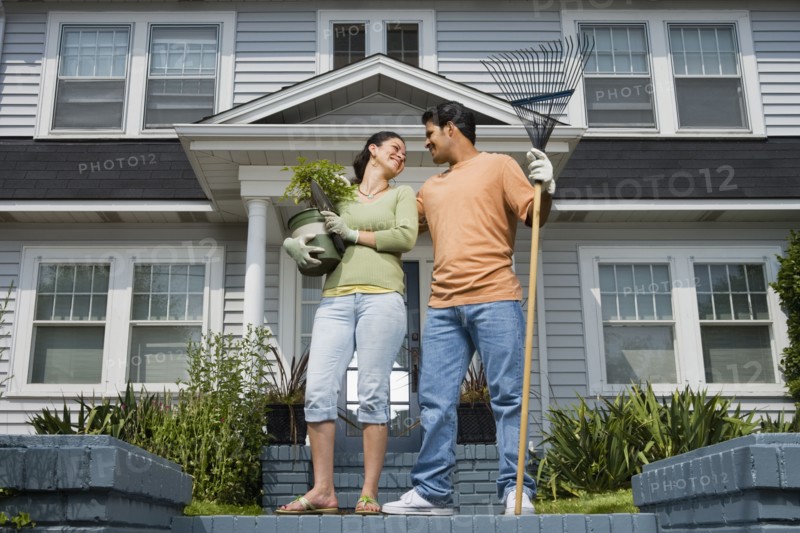 Hispanic couple with gardening tools in front of house