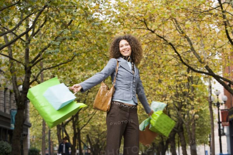 Hispanic woman swinging shopping bags in urban park