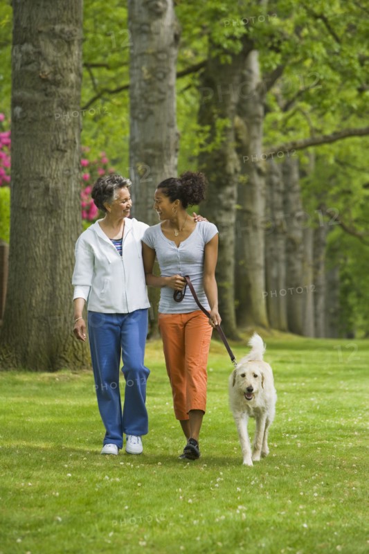 African American mother and adult daughter walking dog