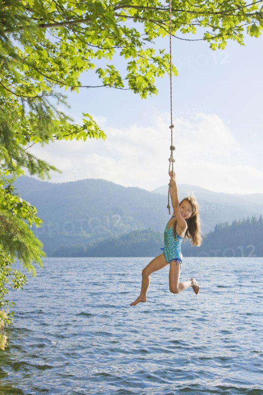 Asian girl hanging from lake rope swing