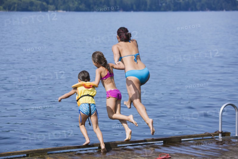 Mother and daughters jumping into lake