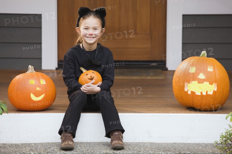 Mixed race young girl in cat costume holding Halloween pumpkin