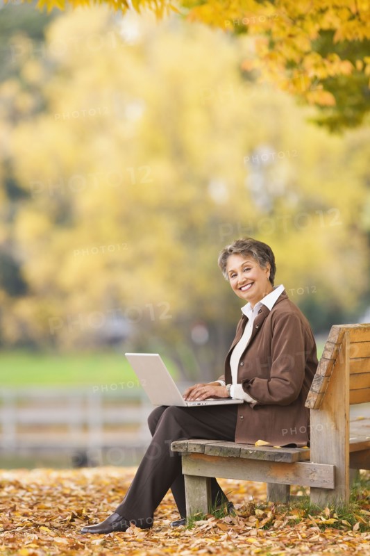 African woman using laptop on park bench in autumn