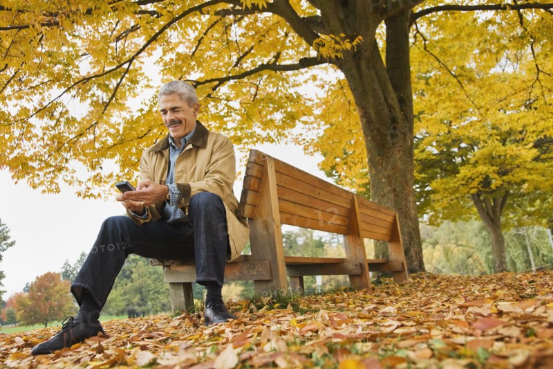 African man using cell phone on park bench in autumn