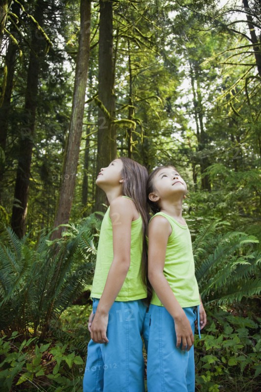 Mixed race girls standing back to back in forest