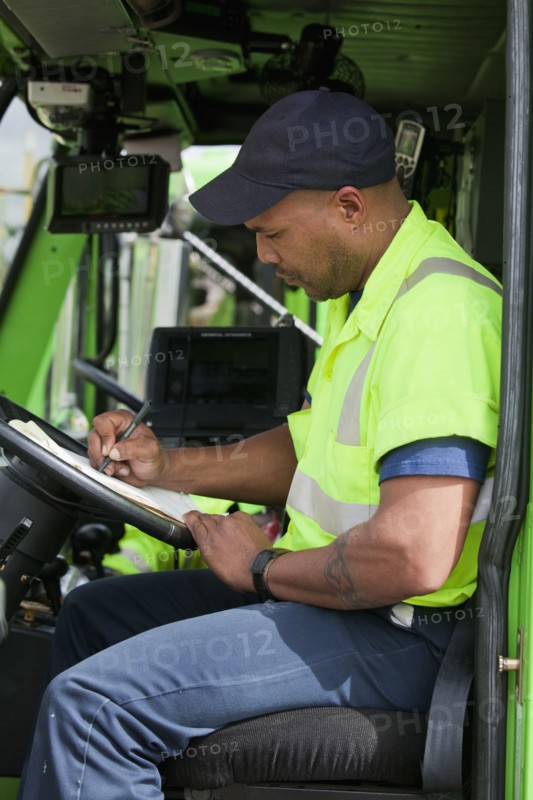 African American man in garbage truck writing on clipboard