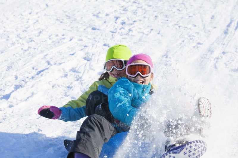 Mixed race girls sledding in snow