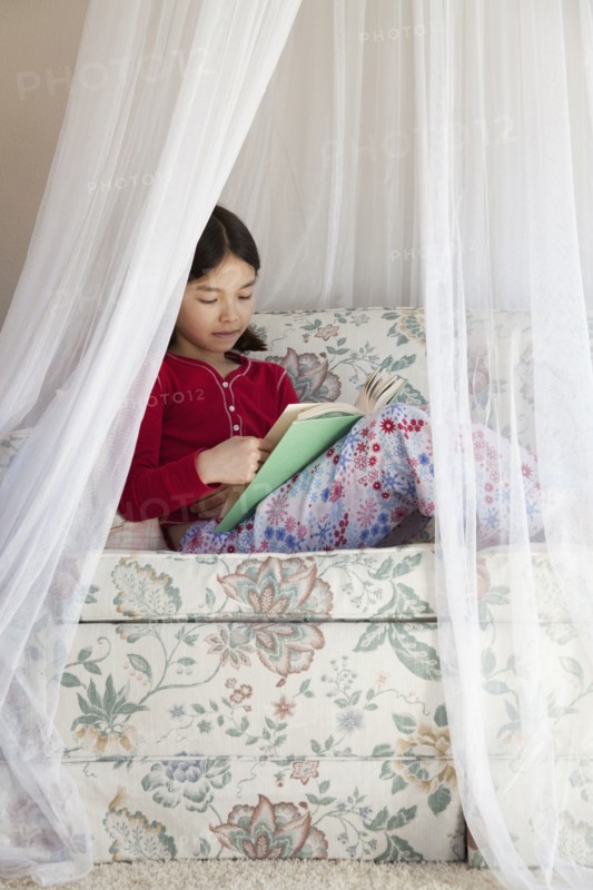 Mixed race girl reading on sofa