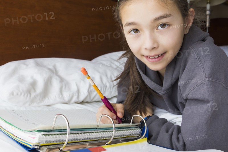 Mixed race girl doing homework on bed