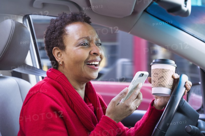 Black woman using cell phone and drinking coffee while driving car