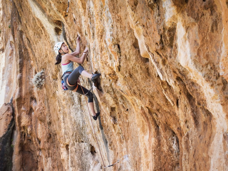 Mixed race girl climbing rock wall