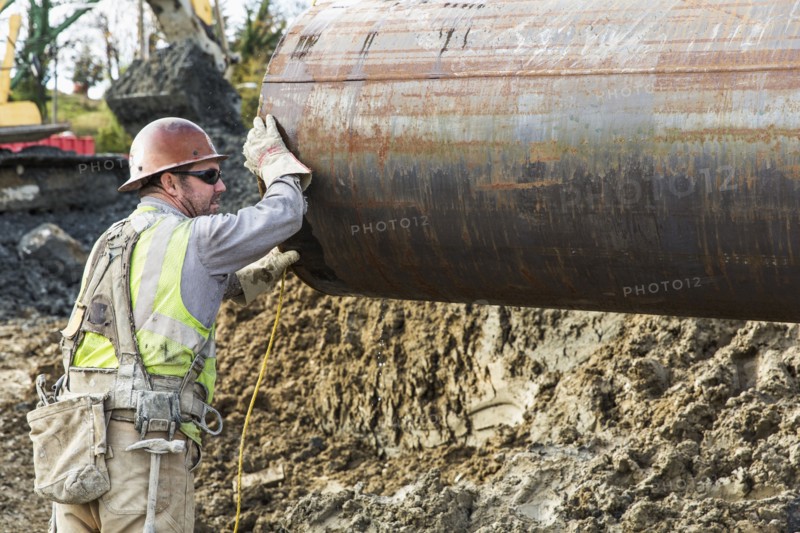 Caucasian worker hauling pipe at construction site