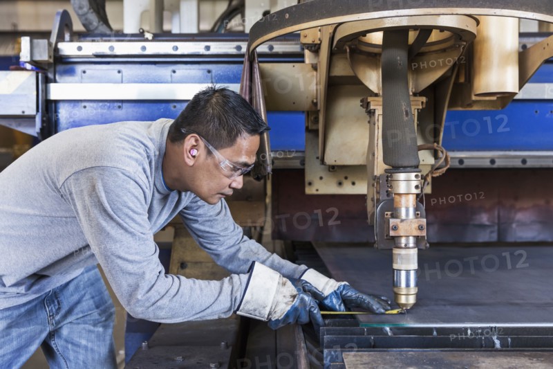 Asian worker fabricating metal in factory
