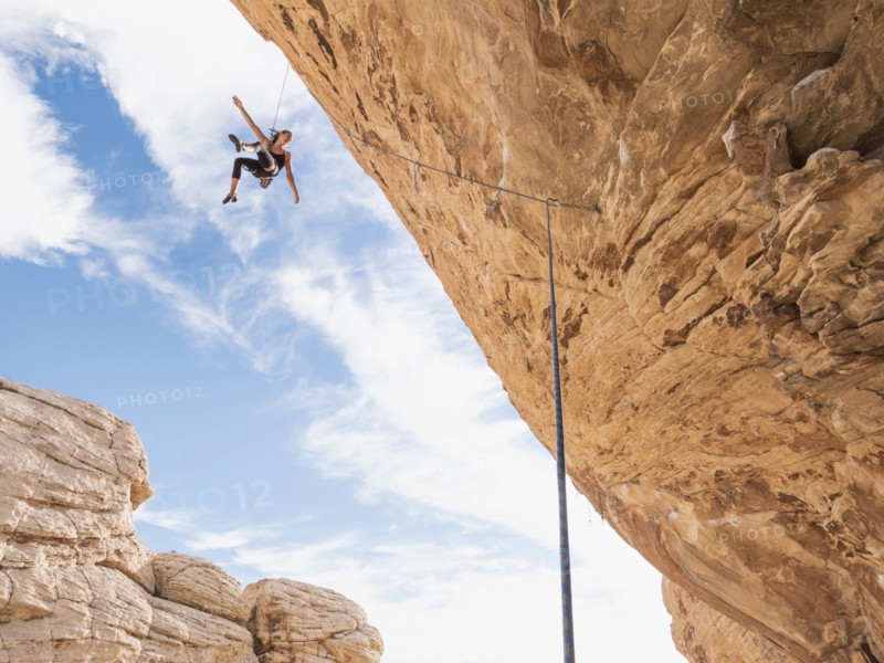 Mixed Race girl hanging from rope while rock climbing