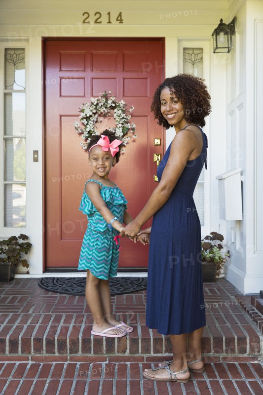 Smiling mixed race mother and daughter standing on front stoop