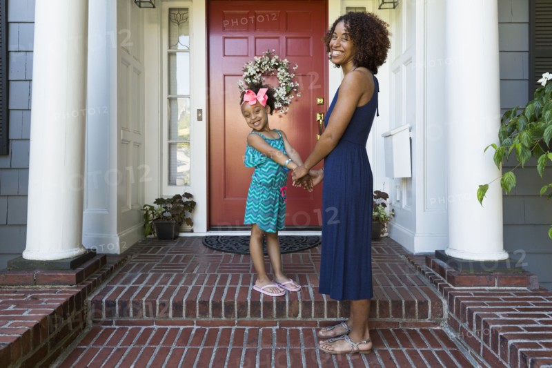 Portrait of smiling mixed race mother and daughter on front stoop