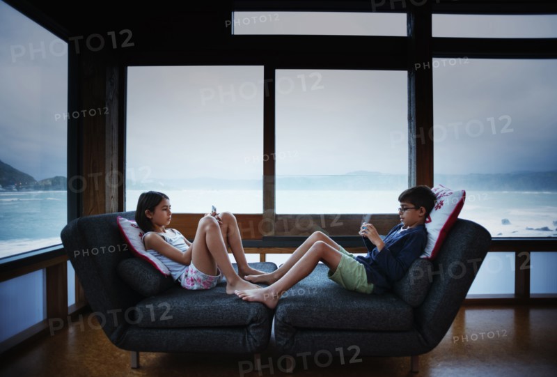 Mixed race children using cell phones in living room