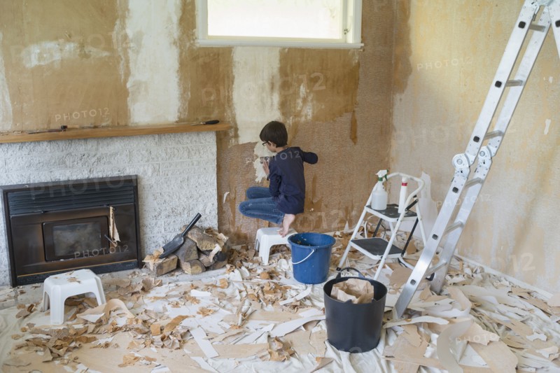 Mixed race boy stripping wallpaper in living room