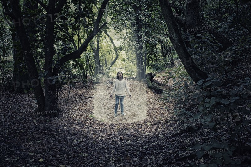 Mixed race girl standing in beam of light in forest