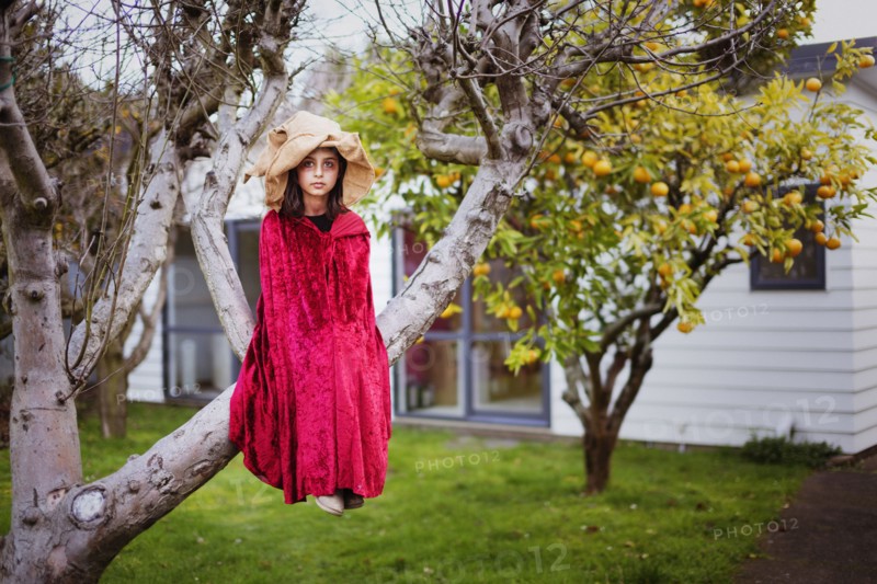 Mixed race girl in witch costume sitting in tree