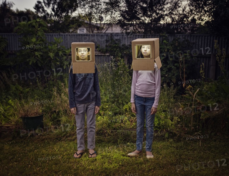 Mixed race children wearing cardboard astronaut helmets in backyard